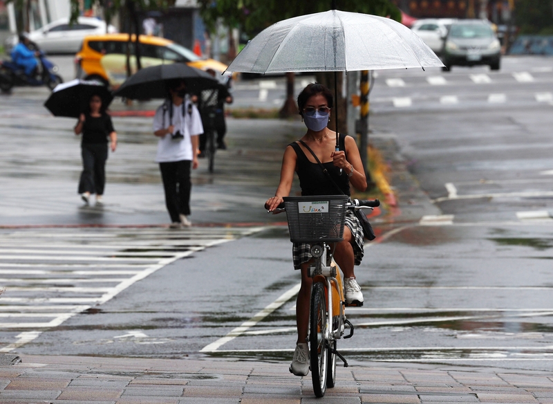 圖為台北市信義區民眾騎腳踏車撐傘遮擋雨勢。（中央社記者張新偉攝）