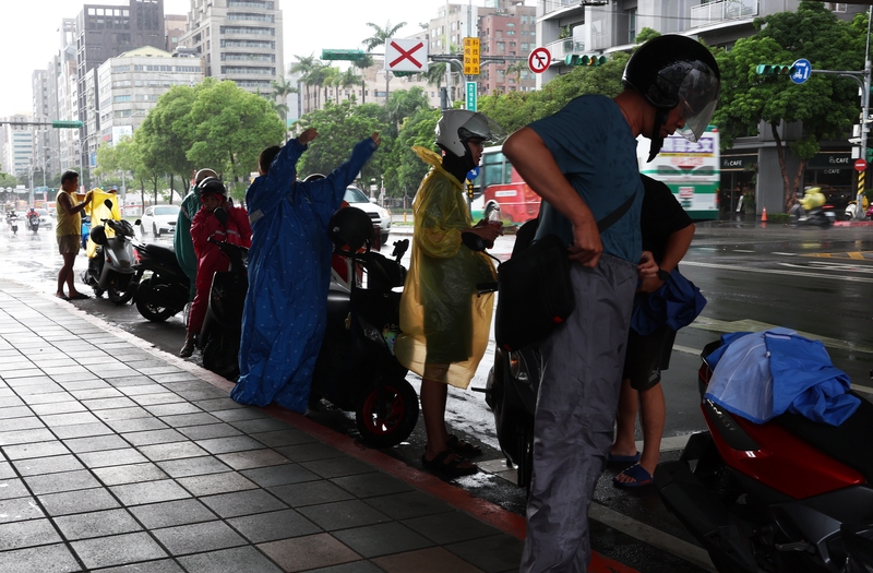 圖為台北市中山區午後降雨，民眾於天橋下急忙穿起雨衣。（ 中央社記者趙世勳攝）